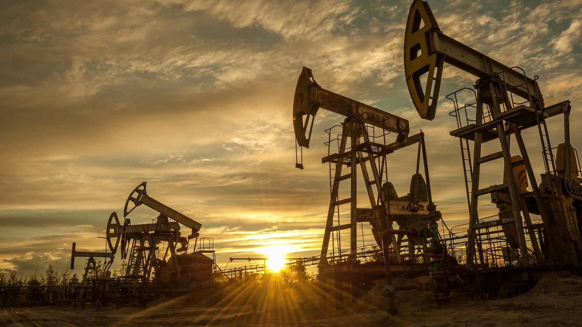 Oil pumps on a fat piece of land with the sun going down in the background