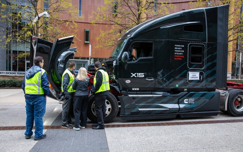Several people inspecting the X15 engine inside of a Cummins branded truck