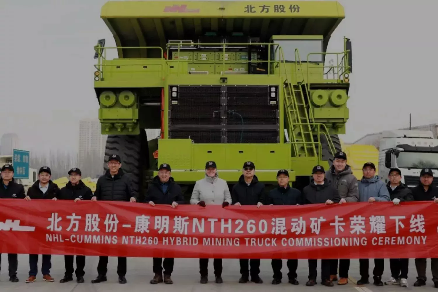 15 cummins workers holding a red banner with the words nhl-cummins nth260 hybrid mining truck commissioning ceremony in front of a large mining vehicle