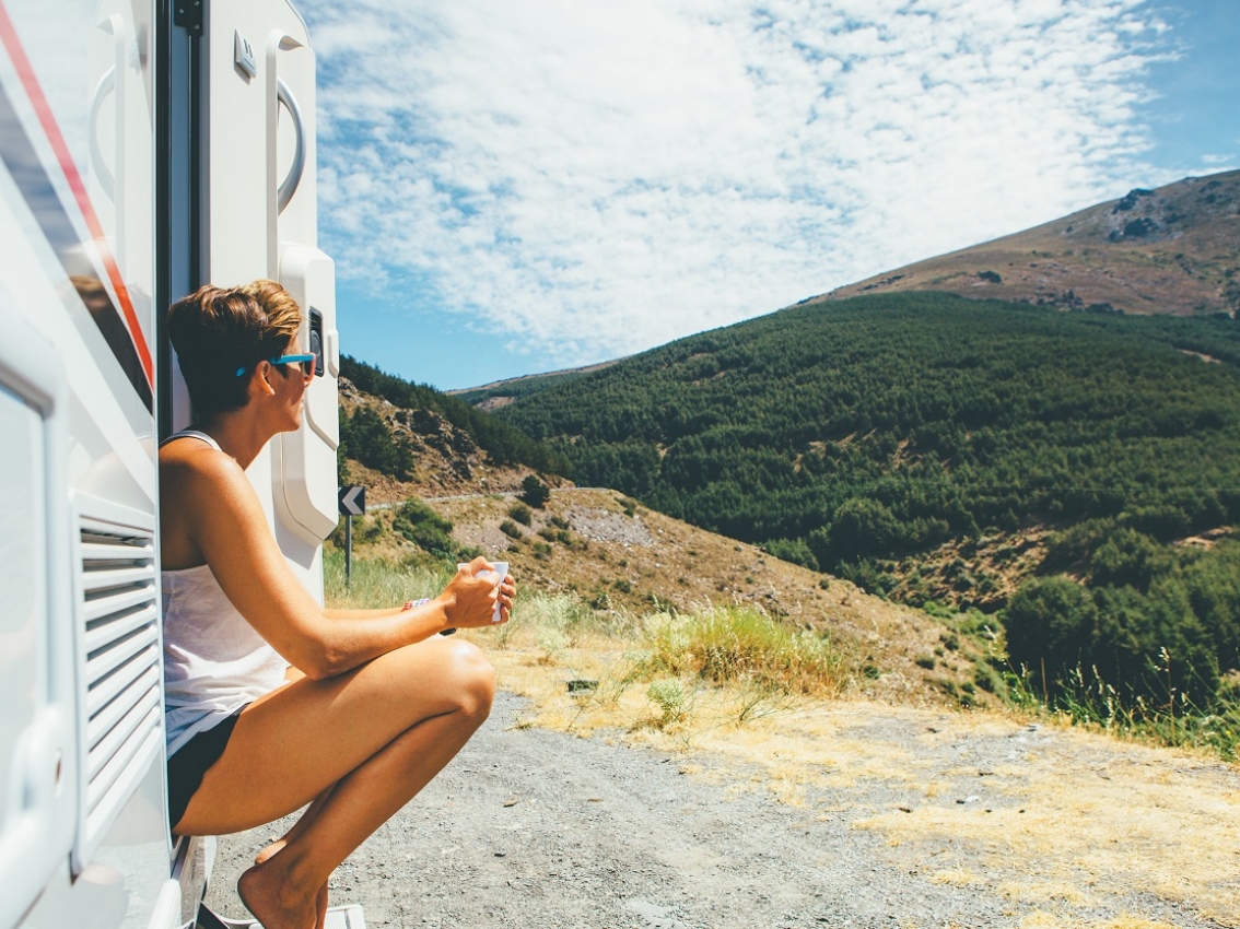 Woman drinking coffee outside her RV looking at a mountain